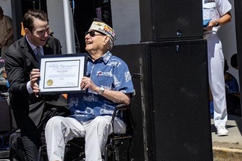 Kevin Kiley kneeling beside Lou Conter, seated in a wheelchair, as the two hold a framed certificate