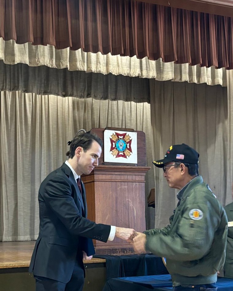 Kevin Kiley shaking hands with a veteran in a cap and flight jacket, in front of a stage
